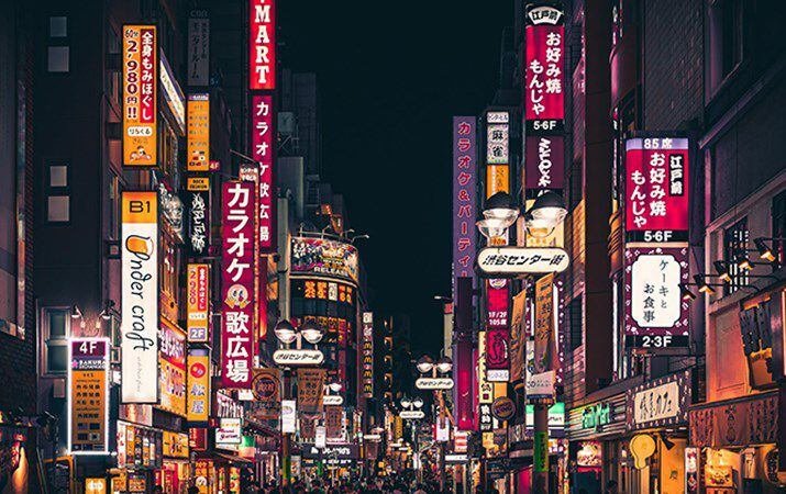 Strada di Tokyo di notte illuminata da numerose insegne al neon con scritte giapponesi.